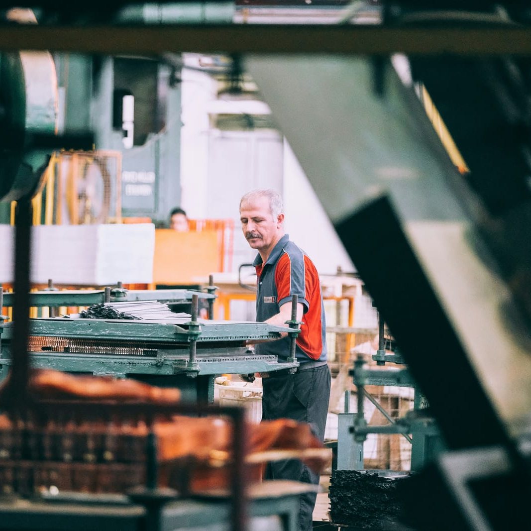 A worker in a red and gray shirt at an industrial machine in a workshop.