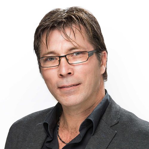 Smiling man with medium-length brown hair, with glasses and wearing a charcoal jacket