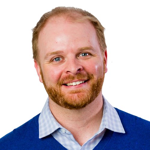 Chris Wood, smiling, with short ginger hair and a beard, in a blue sweater over a checked shirt
