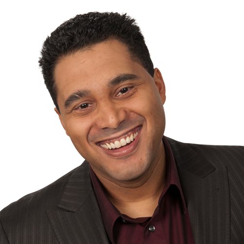 Dan Belhassen, smiling, with short dark hair, in a dark red shirt and charcoal jacket