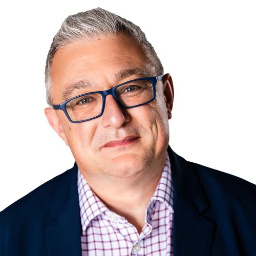 Smiling person with short grey hair and dark-rimmed glasses, in a navy jacket and checked shirt