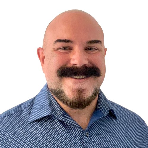 Steve Sakalauskas, smiling, with a shaved head, moustache and beard, in a blue patterned shirt